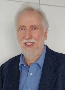 Herr Buhmann mit weißem Haar und Bart, lächelt in dunklem Sakko.